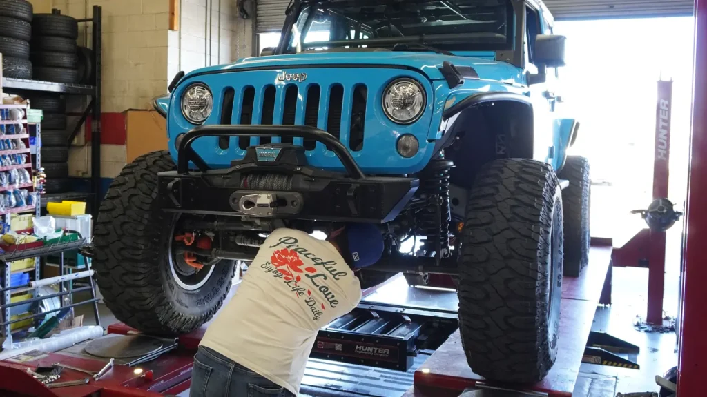 Technician aligning a lifted Jeep on the Hunter alignment rack at Comtires in Ontario, CA
